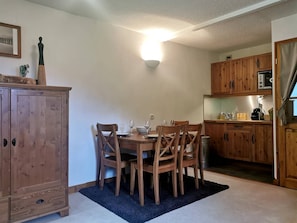 Un coin repas avec une table et des chaises en bois, un buffet et un espace cuisine doté de meubles et d’appareils électroménagers en bois.