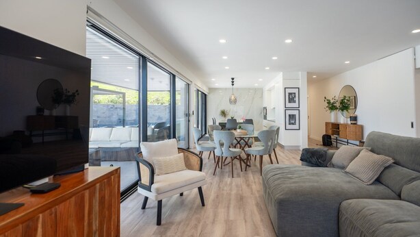 A modern living room with a grey sofa, a wooden cabinet, and a dining area with light blue chairs.