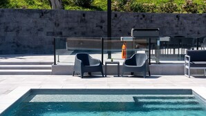 A modern outdoor pool area with a glass railing, two chairs, and a table.