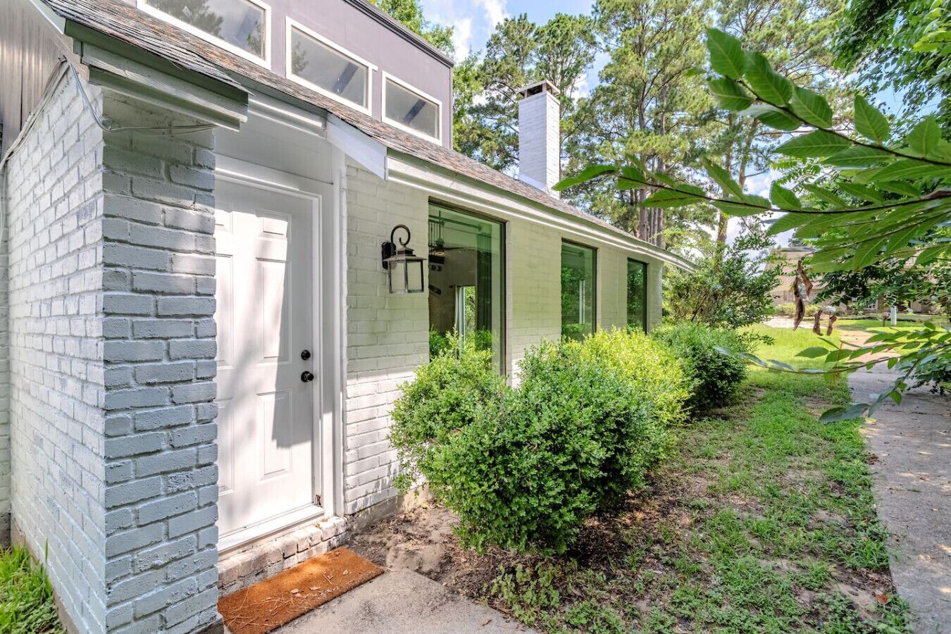 A single-story house with a white exterior, a brick foundation, and a green door.