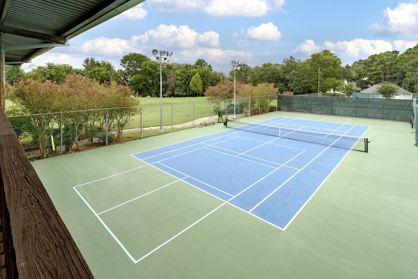 Een tennisbaan buiten met een net, omringd door bomen en een hek.