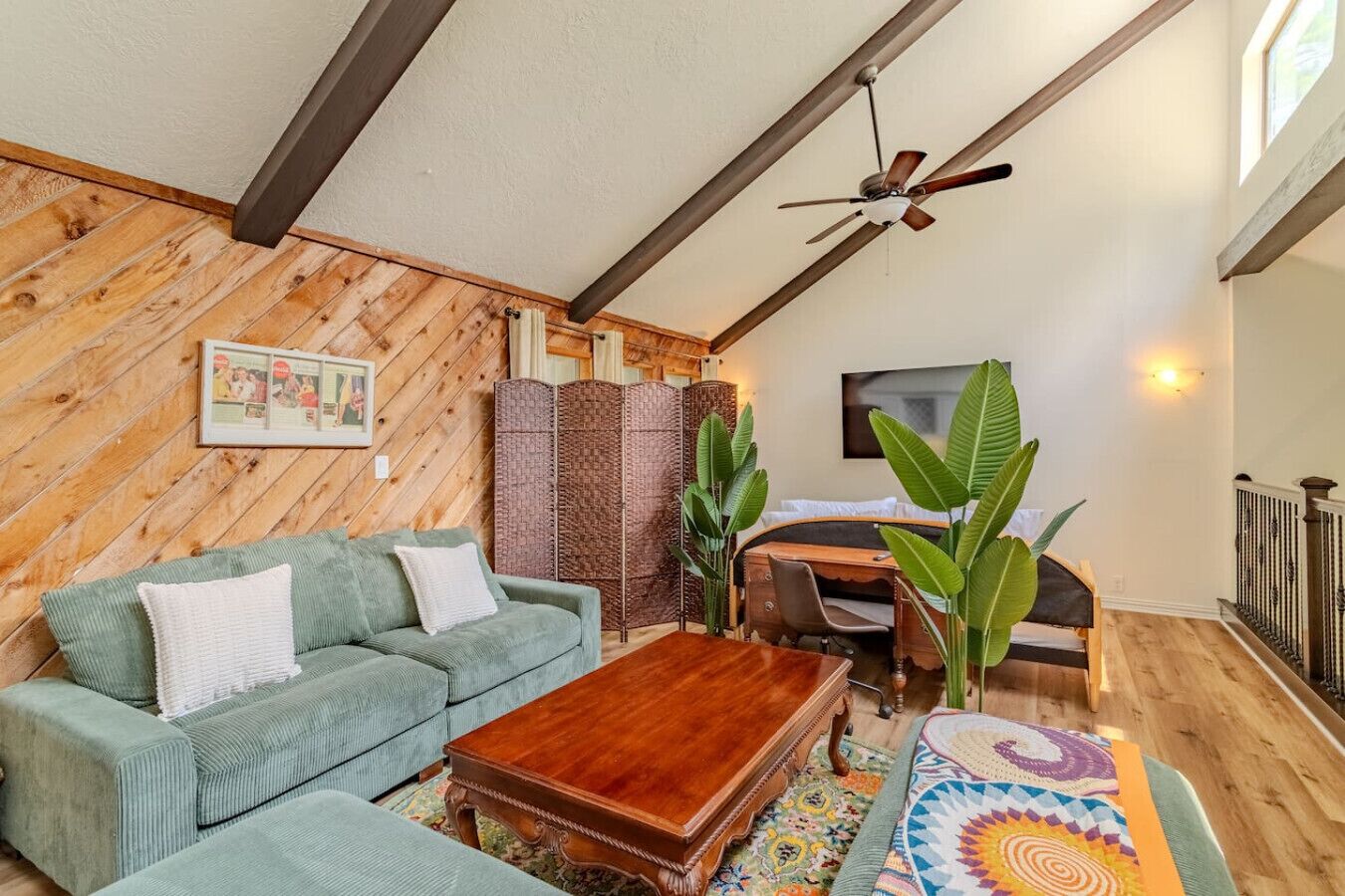Ein gemütliches Wohnzimmer mit Holzbalkendecke, einem grünen Sofa, einem Holztisch und einer großen Pflanze.