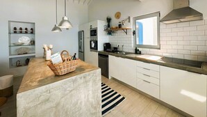 Een moderne keuken met witte kasten, een centraal eiland, hanglampen, een roestvrijstalen afzuigkap en een raam voor natuurlijk licht.