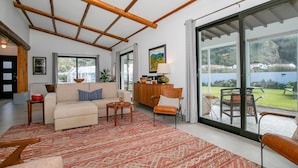 A spacious living room with a high ceiling, a large sofa, a coffee table, and a view of the outdoors through sliding glass doors. - Villa Sun and Sea | Pool n' 2min walk to the Beach (Ponta Delgada)