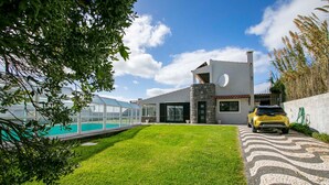 A modern house with a swimming pool, a car parked in front, and a well-maintained lawn. - Villa Sun and Sea | Pool n' 2min walk to the Beach (Ponta Delgada)