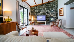 A living room with a stone wall, wooden beams, a television, and a fireplace. - Villa Sun and Sea | Pool n' 2min walk to the Beach (Ponta Delgada)