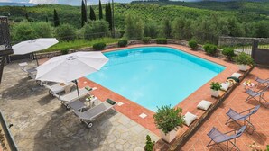 Une piscine rectangulaire dotée d’une terrasse en pierre et offrant une vue sur un paysage verdoyant luxuriant.