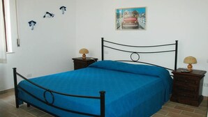 Une chambre à coucher avec un lit en métal, une couvre-lit bleue, deux tables de chevet avec des lampes et un tableau accroché au mur.
