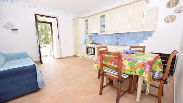 Une pièce confortable avec un lit, une table à manger et des chaises, une cuisine avec des meubles blancs et une vue par une porte.