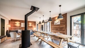 A modern dining area with wooden tables and benches, a black central column, and pendant lighting.
