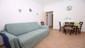 Un saló amb un sofà, una taula de dinar amb cadires, i una porta que condueix a una altra habitació.