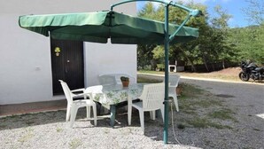 Un pati amb taula i cadires, un parasol verd i una moto aparcada a prop.