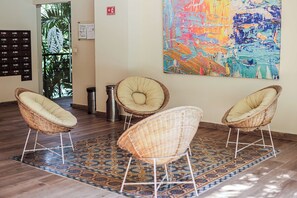 Un hall con tres sillones de mimbre, un tapete estampado, un cuadro abstracto grande y un letrero de salida de incendios.