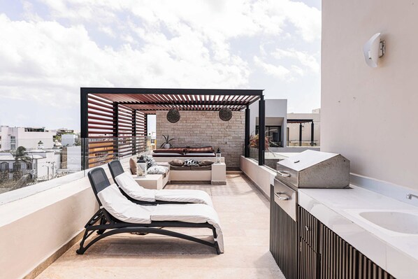 Una terraza en la azotea con zona de estar, una parrilla y vistas a la ciudad.