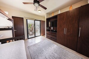 A bedroom with a bed, a ceiling fan, a wardrobe, and a sliding glass door leading to a balcony.