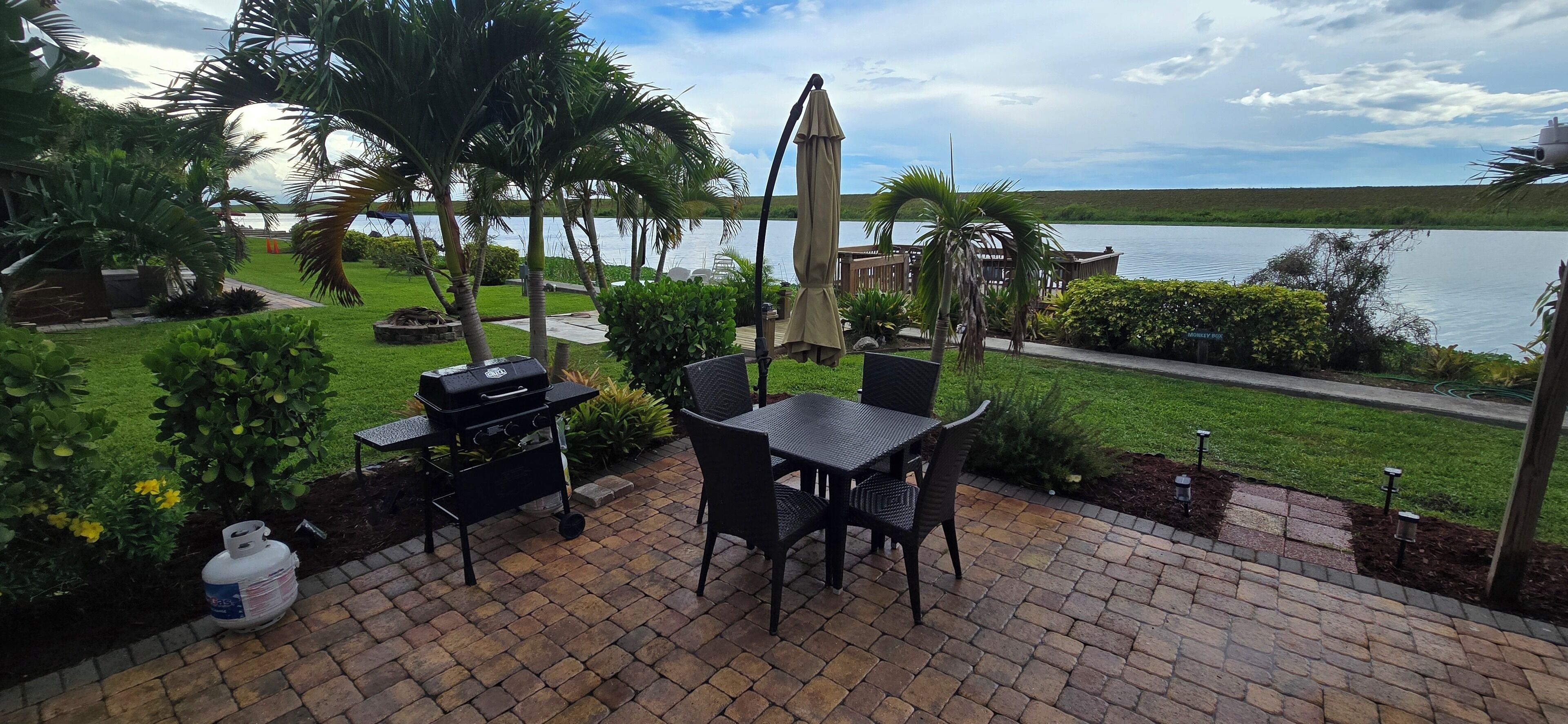An outdoor patio with a grill, dining table, chairs, and a view of a lake.