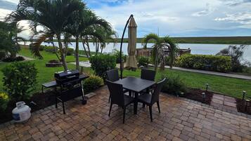An outdoor patio with a grill, dining table, chairs, and a view of a lake.