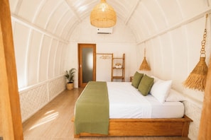Una habitación con una cama, una lámpara colgante, un estante de madera y una planta en maceta.