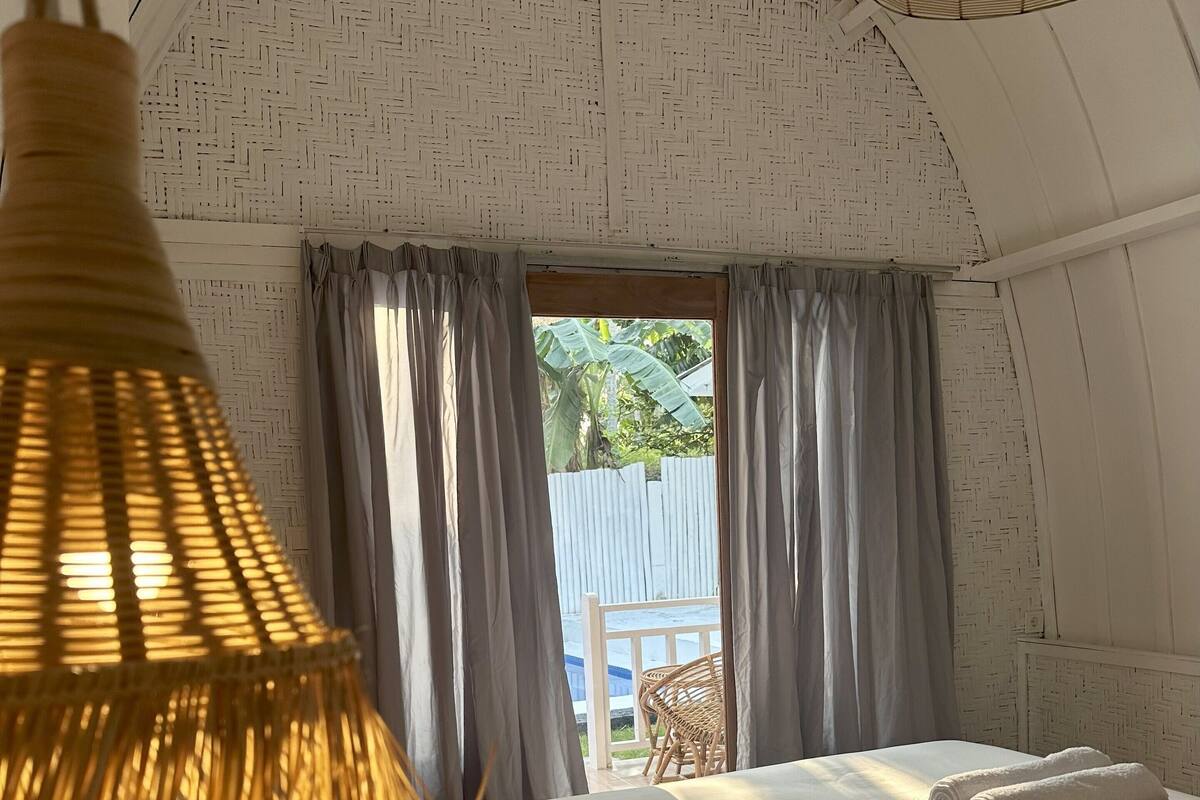 A cozy bedroom with a bed, curtains, and a hanging lamp.