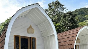 Twee witte, halfronde, gelijkvloerse gebouwen met houten deuren en ramen, elk met een klein terras en een witte balustrade.