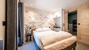 Un dormitorio con cama, mesita de noche, armario de madera y una pared con un mural de montañas.