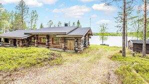 A rustic log cabin with a metal roof, surrounded by a natural landscape and a lake. - Lumikenttien kutsu by Interhome (Kuusamo)