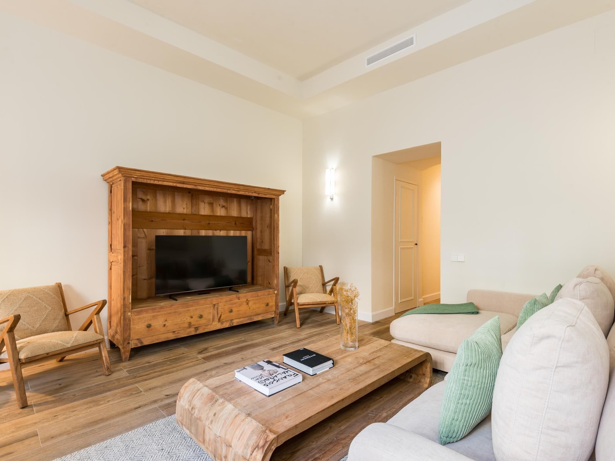 Una sala de estar con un mueble de madera para entretenimiento, un televisor de pantalla plana, dos sillones, un sofá y una mesa de centro con libros.