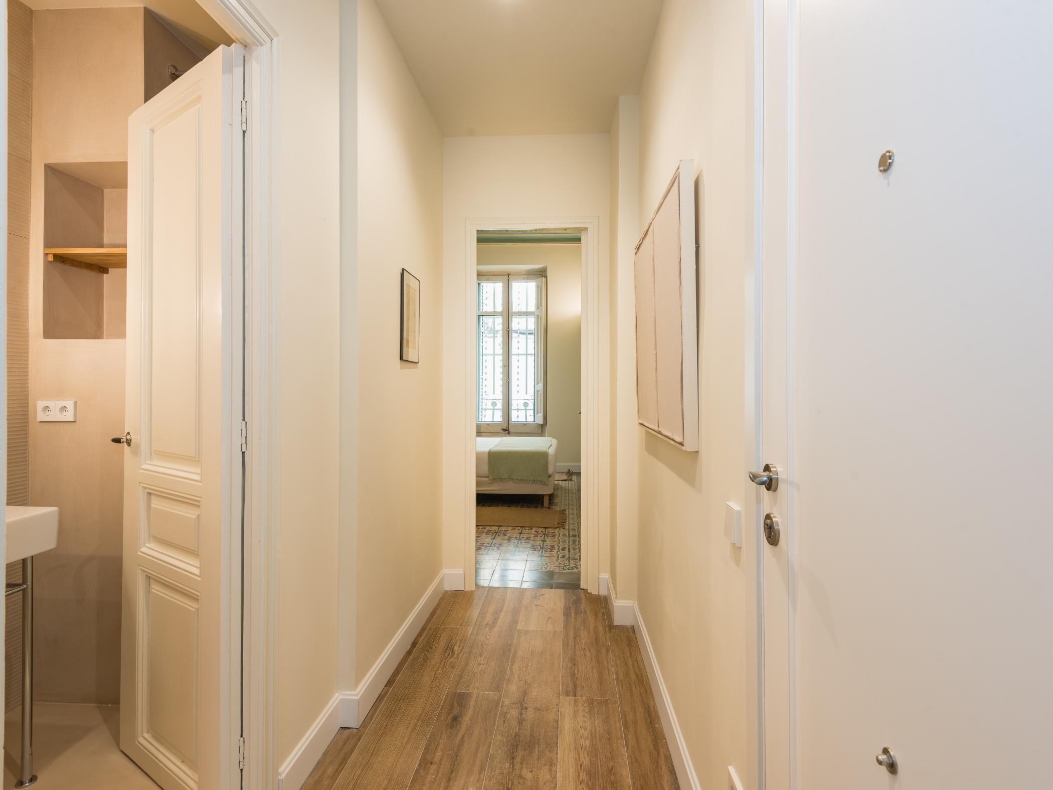 A hallway with wooden flooring, white walls, and doors leading to different rooms.