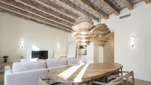 A modern living room with a large wooden dining table, light-colored sofa, and wicker chairs. - The Residences At Bartomeu 26, Suite Maricel, Spacious Elegance & Comfort (Sitges)