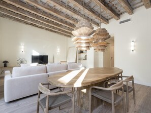 A modern living room with a large wooden dining table, light-colored sofa, and wicker chairs.