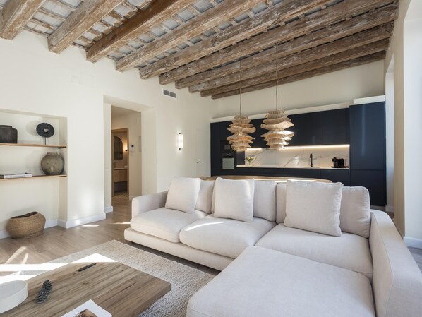 Una sala moderna con un amplio sofá seccional color beige, una mesa de centro de madera y un techo rústico.