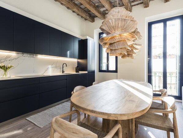Una cocina moderna con armarios oscuros, encimera de mármol y una mesa redonda de madera con sillas.
