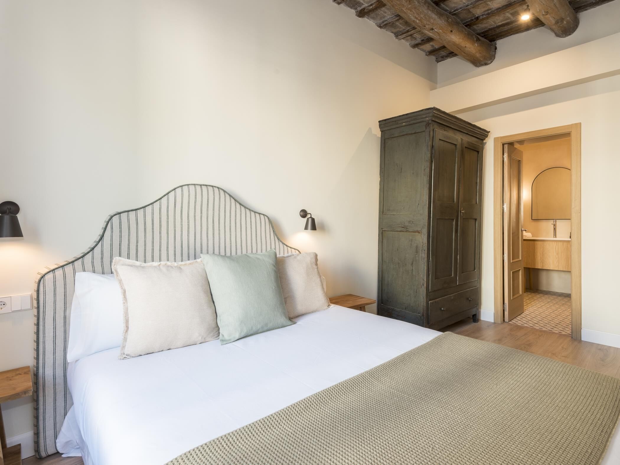 A bedroom with a bed, bedside lamps, a wardrobe, and a bathroom visible through an open door.