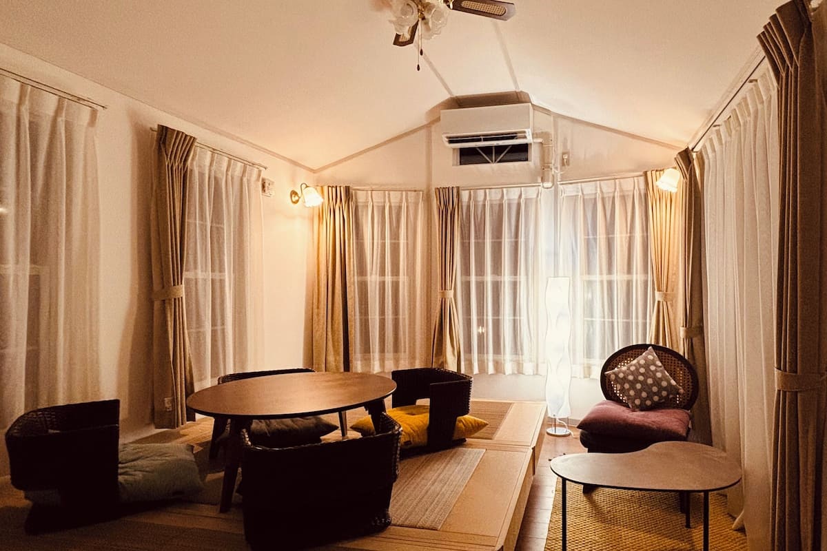 Un salon chaleureux avec une table ronde, un canapé et un fauteuil. On y trouve également un ventilateur de plafond et un appareil de climatisation.