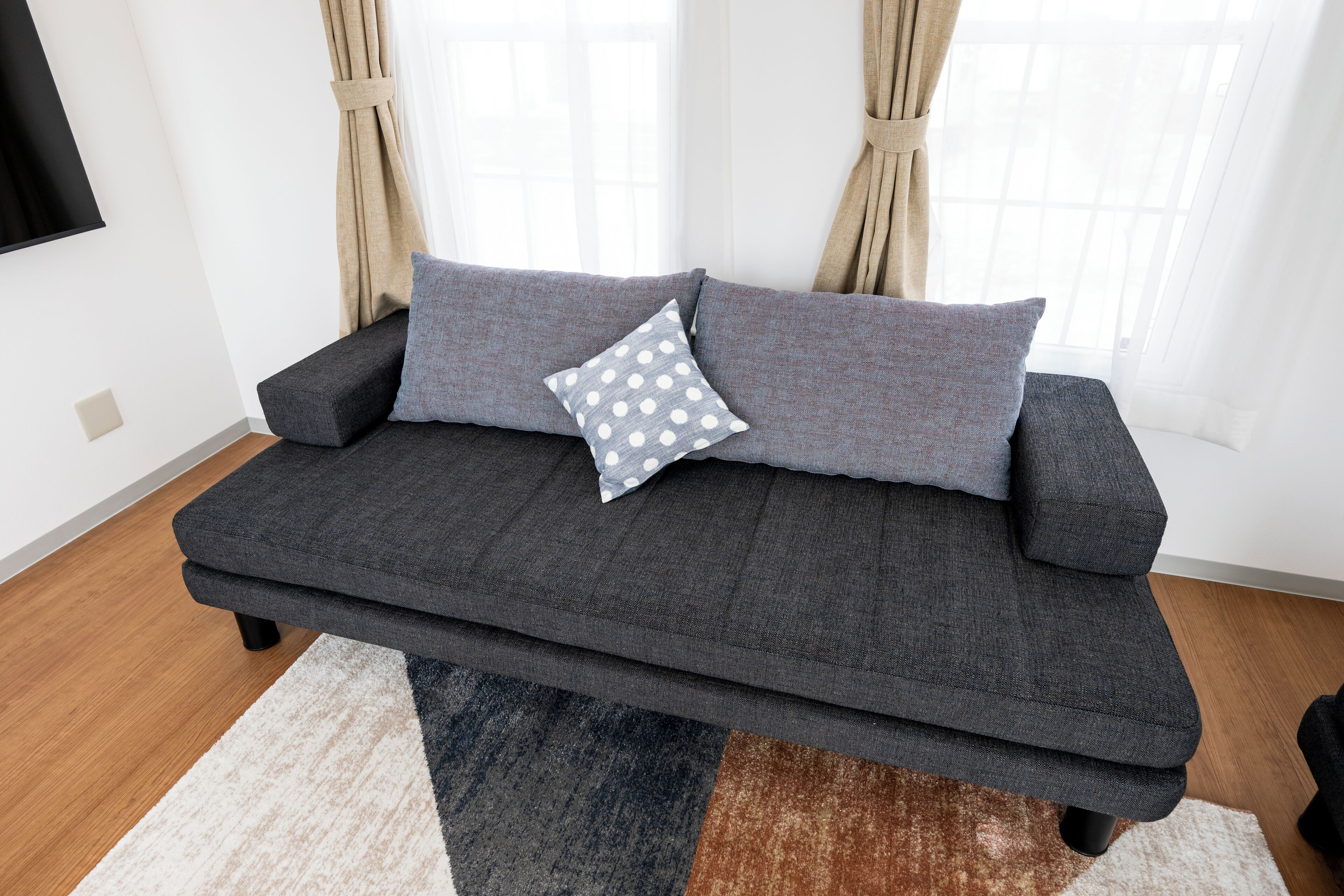 A modern living room with a grey sofa, two cushions, and a patterned rug.