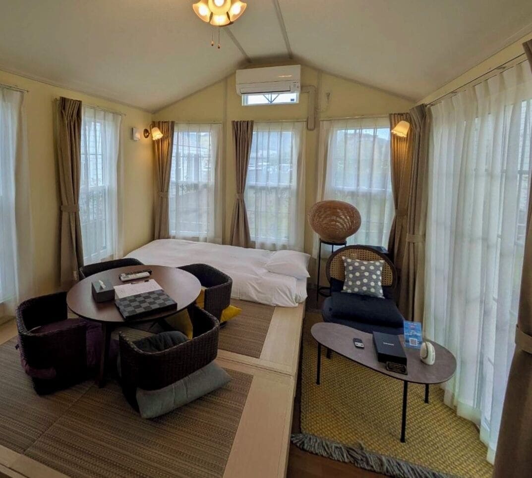 A hotel room with a bed, two seating areas, a small table, and an air conditioning unit.