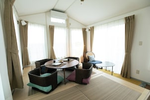 Una sala de estar moderna con una mesa redonda, muebles de mimbre y vistas al exterior a través de ventanas amplias.