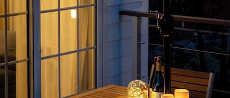 An outdoor patio with a wooden table, chairs, a lantern, candles, and a bottle of wine.
