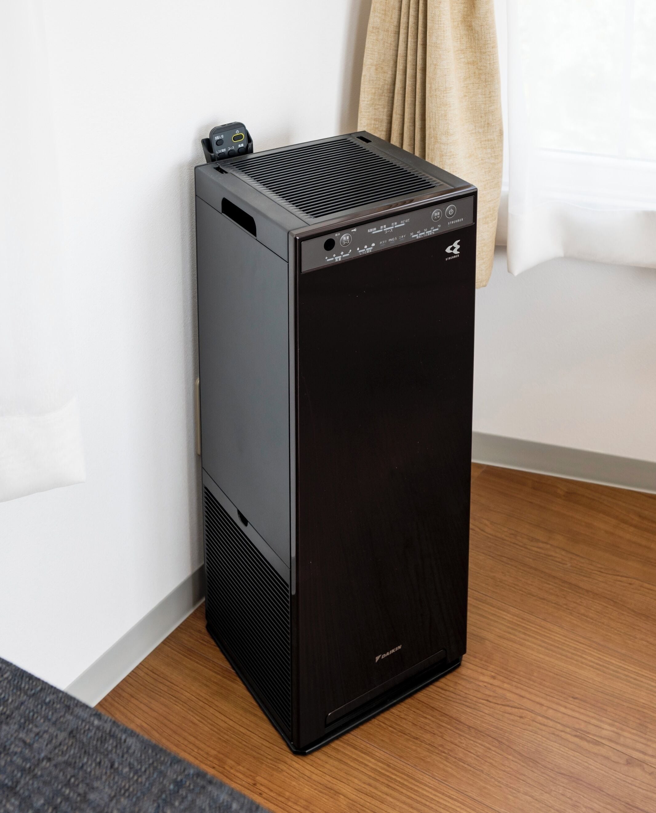 A black portable heater with a control panel and a power cord, placed on a wooden floor against a white wall.