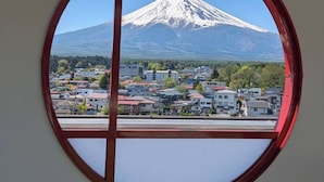 A view through a circular window of a snow-capped mountain and a town below. - Inn the Fuji (Fujiyoshida)