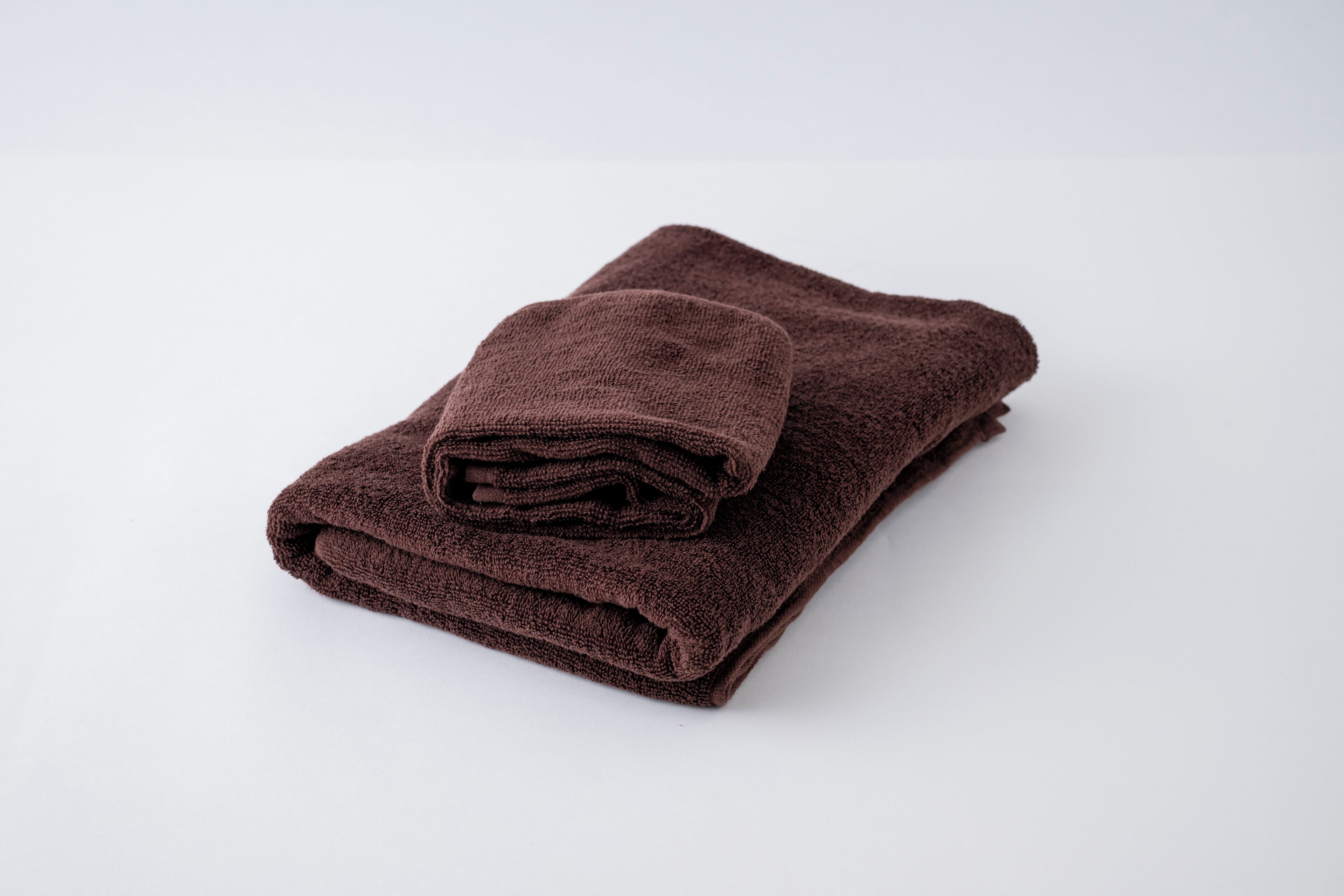 A folded brown towel on a white surface.