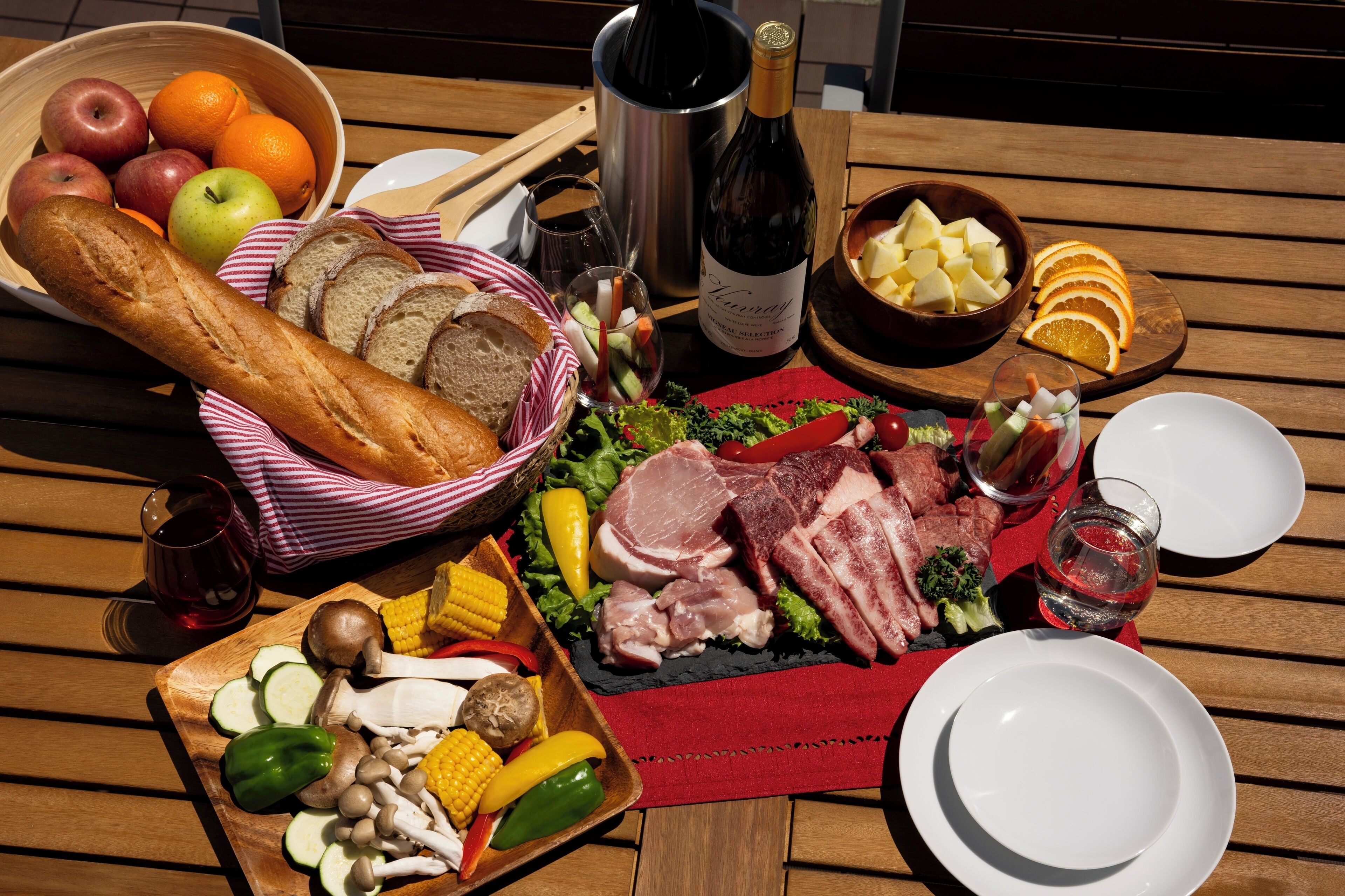 A wooden table with a variety of food items, including bread, fruits, vegetables, and meats, along with bottles of wine and glasses.