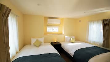 Quarto de hotel com duas camas, uma janela com cortinas, um ar condicionado e uma mesa de cabeceira com abajur.