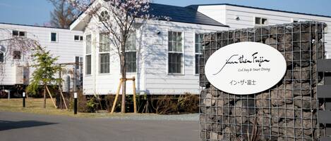 A sign for 'Jim the Fuji' with a stone wall backdrop, a white building with windows, and a tree with pink blossoms.