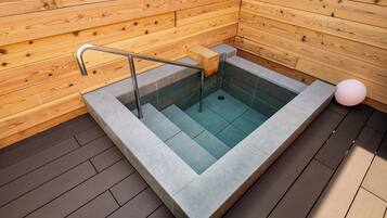 A wooden sauna with a glass-enclosed hot tub, a metal handrail, and a pink spherical light.