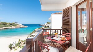 A balcony with a table set for two, overlooking a beach and the sea. - Holidays in Mallorca: renovated apartment with sea views (Portocolom)