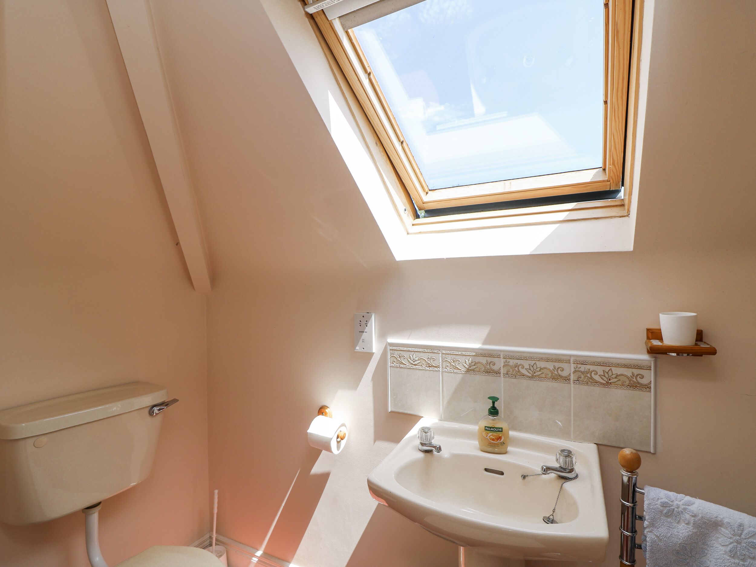 A bathroom with a skylight, toilet, sink, and towel rack.