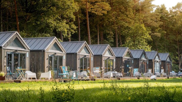 A row of wooden cabins with metal roofs, each with a glass door and windows, surrounded by greenery and trees. - Holiday Home With sea View in Ustronie Morskie (Ustronie Morskie)
