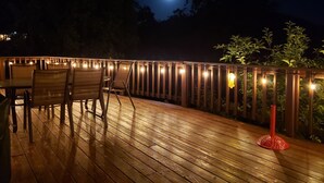 Une terrasse en bois avec des chaises et des tables, des guirlandes lumineuses et un objet décoratif rouge.