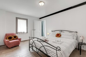 Un dormitorio con cama, una silla, una mesita de noche y una ventana.
